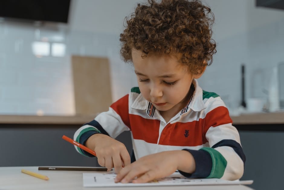 A young child focused on drawing with colored pencils at a table indoors, displaying creativity and concentration.
