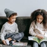 Siblings reading a picture book together indoors, fostering a love of literature.