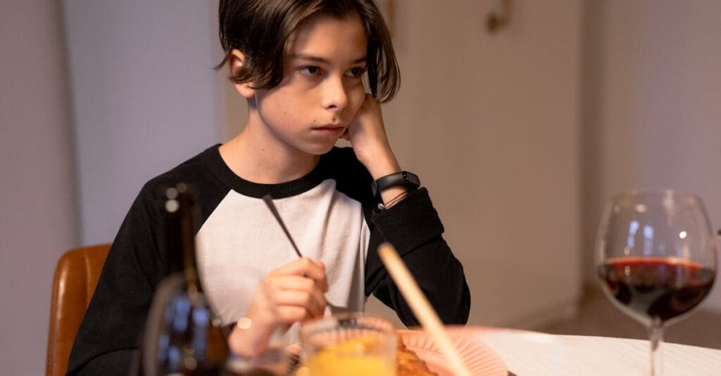 Teenage boy sitting at a dining table, appearing thoughtful during dinner indoors.