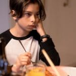 Teenage boy sitting at a dining table, appearing thoughtful during dinner indoors.