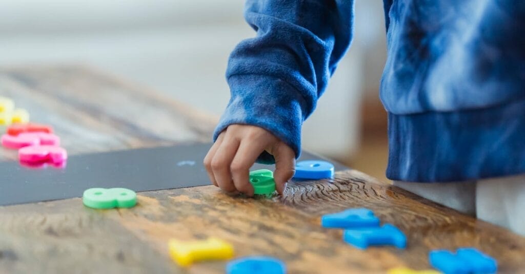 Crop anonymous ethnic boy taking plastic number from wooden table while learning math