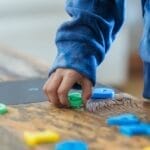 Crop anonymous ethnic boy taking plastic number from wooden table while learning math