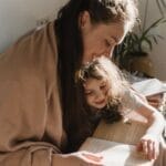 A warm moment of a mother and daughter reading a book by the window.