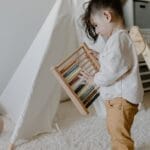 Young child learns with a wooden abacus in a cozy, indoor playroom setting.