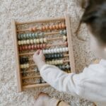 A young child interacting with a colorful wooden abacus on a light carpet, viewed from above.