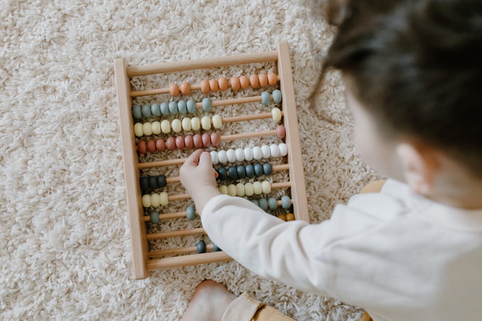 A young child interacting with a colorful wooden abacus on a light carpet, viewed from above.