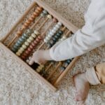 A young child interacts with a colorful wooden abacus, exploring learning through play.