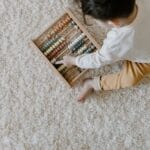 Young child playing with a colorful wooden abacus on a carpet.