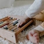 Toddler engaging with a wooden abacus on a fluffy carpet, promoting early learning.