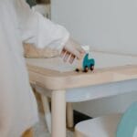 A young child plays with a wooden toy on a small table indoors, showcasing minimalist design.