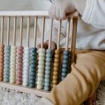 A young child engaging in learning with a wooden abacus on a carpet, emphasizing early education.