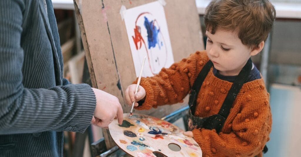 Young boy learning to paint with teacher's guidance during art class.