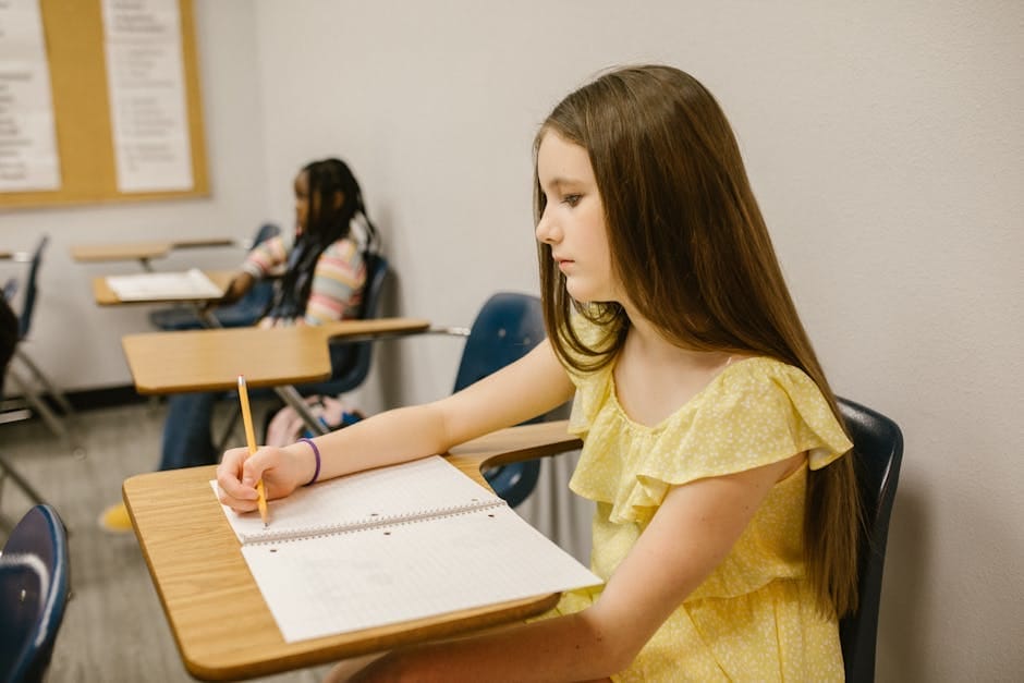 A young girl sitting alone in a classroom, studying and writing in a notebook.