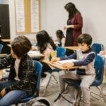 Engaged students in a classroom setting with attentive teacher guidance.