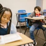 Students in a classroom setting, focused on their books and smartphones.