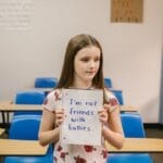 A girl stands in an empty classroom holding an anti-bullying sign.