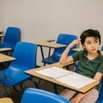 A young boy appears thoughtful while sitting alone in a classroom.