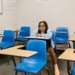 A young girl sits alone in an empty classroom, symbolizing bullying and solitude.