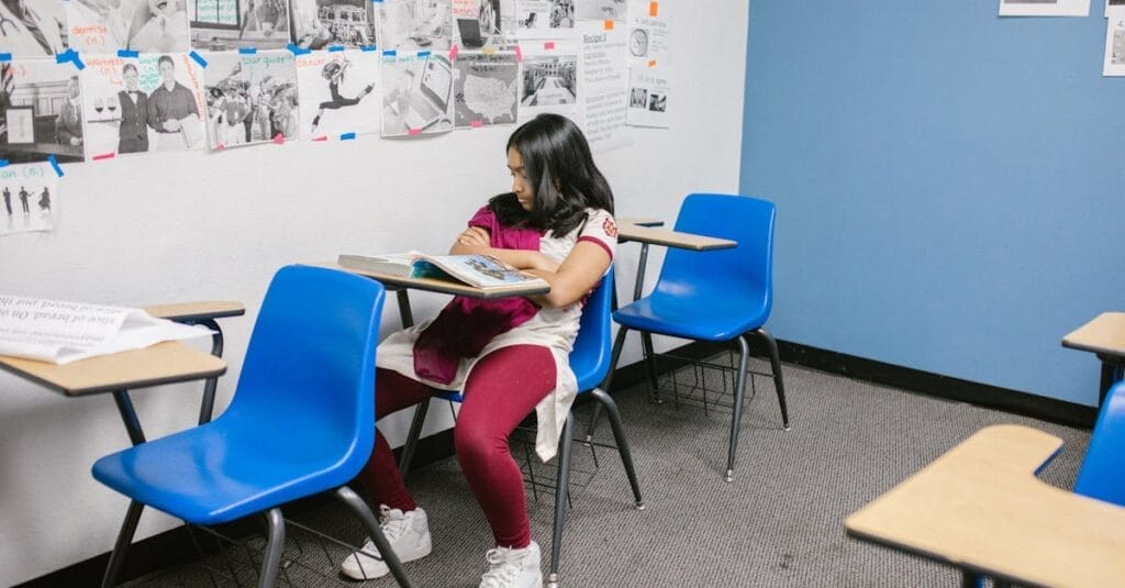 Young girl sitting alone in a classroom with blue chairs, symbolizing bullying and isolation.