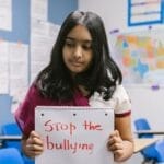 A schoolgirl holds a 'Stop the bullying' sign in a classroom to raise awareness against bullying.