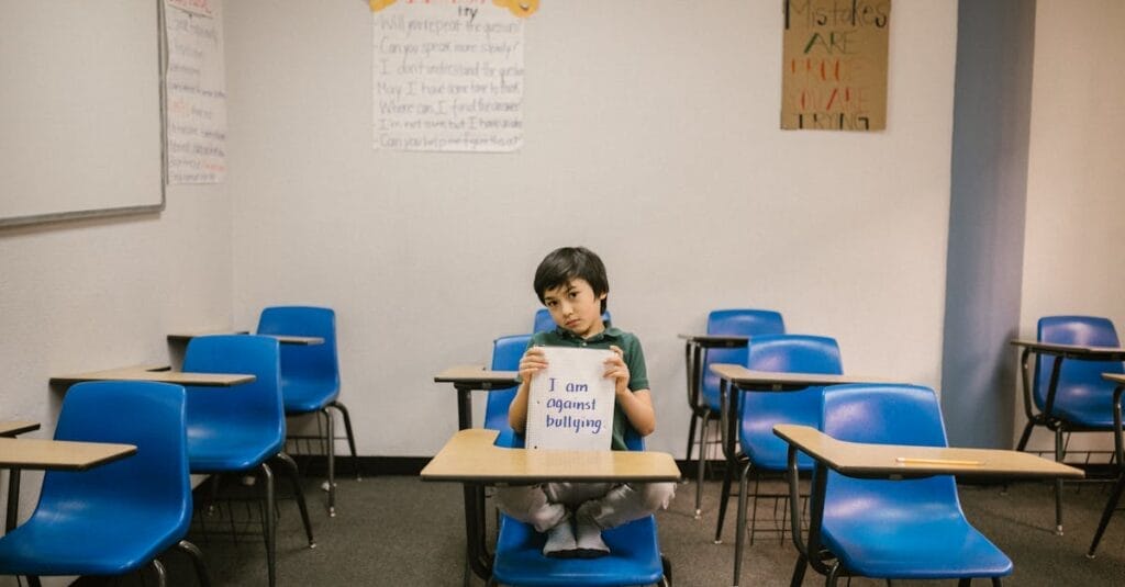 A child sits in an empty classroom, holding a sign against bullying.