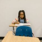 A young girl sits alone in a school classroom, symbolizing the impact of bullying.