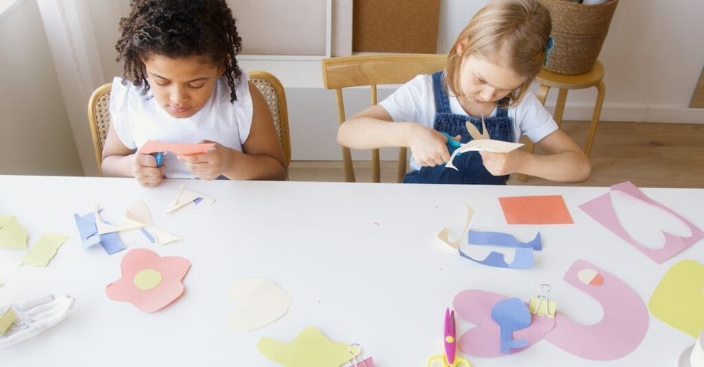 Two children crafting colorful paper shapes, focusing on creativity and fun in an indoor setting.