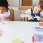 Two children crafting colorful paper shapes, focusing on creativity and fun in an indoor setting.