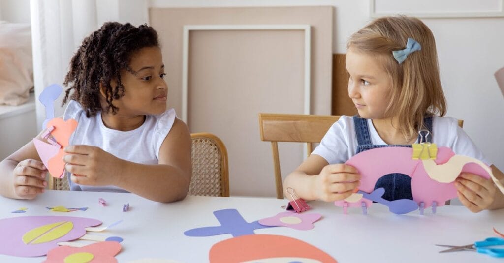 Two children having fun with arts and crafts, creating paper cutouts indoors.