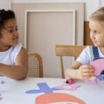 Two children having fun with arts and crafts, creating paper cutouts indoors.