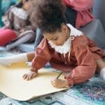 Child drawing on paper in an indoor art setting, fostering creativity.