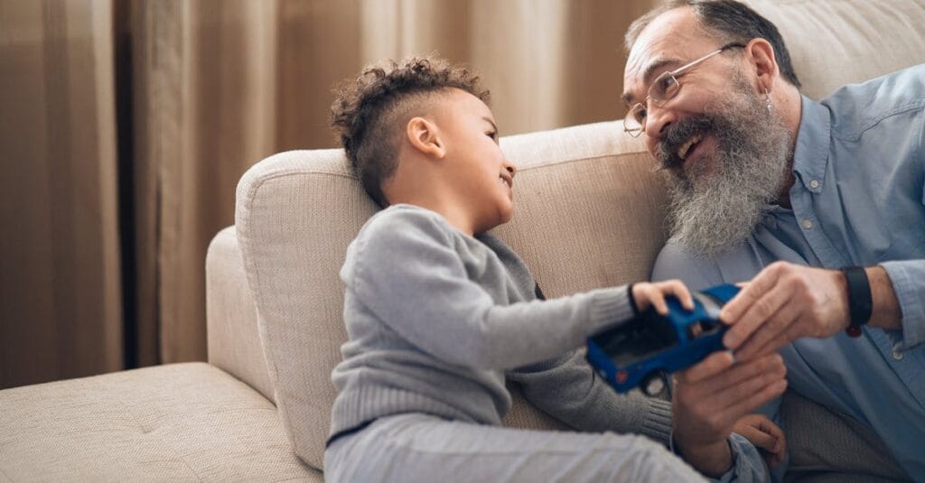 A joyful grandfather and grandson sharing a playful moment on the couch, indoors.