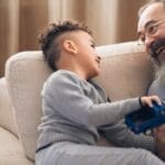 A joyful grandfather and grandson sharing a playful moment on the couch, indoors.