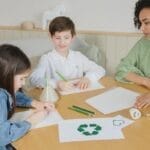 Kids with a teacher learning about recycling at a table indoors.