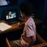 A child participating in an online learning session at a home desk with a laptop.