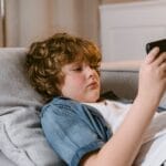 Young boy relaxing on a sofa, using a smartphone, indoors.