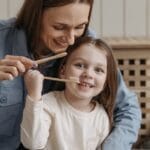 A joyful moment of a mother helping her daughter brush teeth indoors.