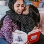 A loving mother and daughter share a tender moment reading together on a cozy bed.