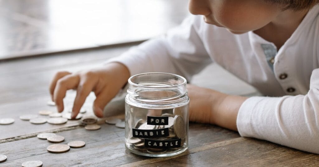 A young child collects coins in a jar labeled 'For Barbie Castle', symbolizing saving and dreams.