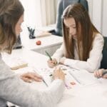 Woman teaching two girls in a bright office environment, focusing on an educational task together.