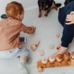 A mother and her child playing with wooden blocks on the floor with their pet dog. Perfect for family and lifestyle themes.