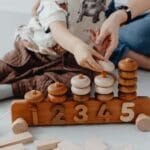 A mother and child engage in playful educational activities with wooden toys, focusing on numbers.