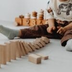 A young child playing with wooden blocks on a light floor, creating a playful and educational scene.