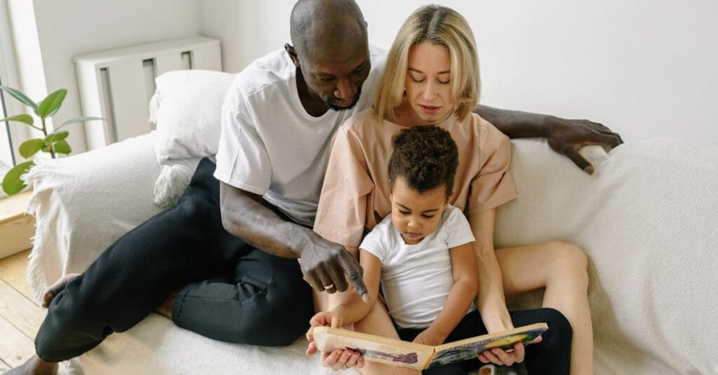 A family enjoys reading time together on a cozy white sofa indoors.