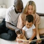 A family enjoys reading time together on a cozy white sofa indoors.