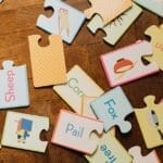 A scattered collection of educational puzzle pieces showcasing words and images on a wooden floor.