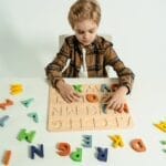 Young boy playing with colorful wooden alphabet puzzle on white table, enhancing learning experience.