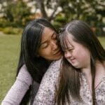 A loving mother embraces her daughter with Down syndrome in a serene outdoor setting.