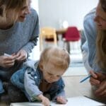 A heartwarming moment of two women and a baby drawing together indoors, symbolizing family bonding.