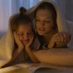 A mother and daughter sharing a cozy bedtime story under a blanket, creating a warm and loving atmosphere.